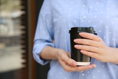 Woman with takeaway coffee cup outdoors, closeupの写真素材