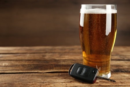 Car key near glass of alcoholic beer on wooden table, space for text. Dangerous drinking and drivingの写真素材