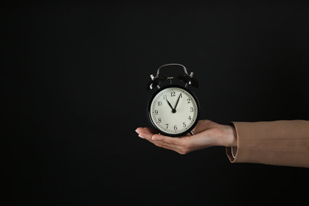 Businesswoman holding alarm clock on black background, closeup with space for text. time managementの写真素材