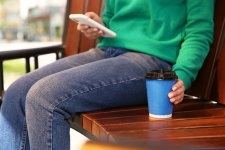 Woman with takeaway coffee cup on bench, closeupの写真素材