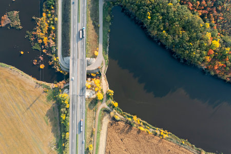 Aerial view of road bridge across river near beautiful autumn forestの写真素材