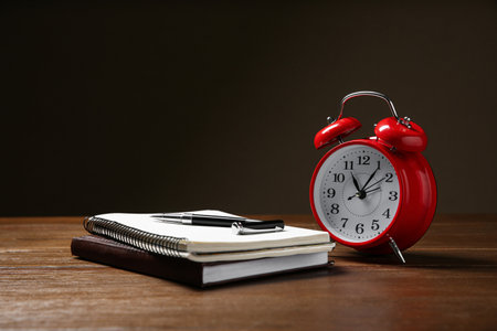 Alarm clock and office stationery on wooden table against dark background, space for text. time...