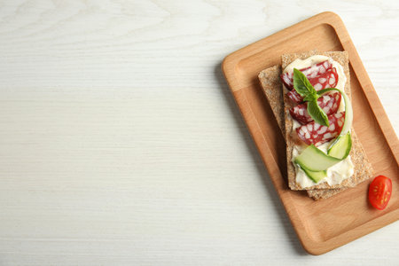 Fresh rye crispbreads with salami, cream cheese and cucumber on white wooden table, top view. Space for textの写真素材