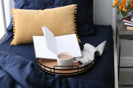 Cup of coffee and notebook on bed with fresh lines indoors