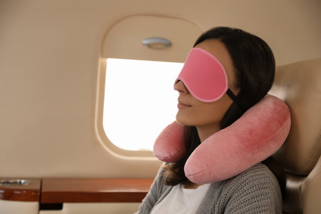 Young woman with travel pillow and mask sleeping in airplane during flightの写真素材