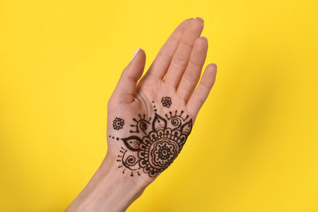 Woman with henna tattoo on palm against yellow background, closeup. traditional mehndi ornamentの写真素材