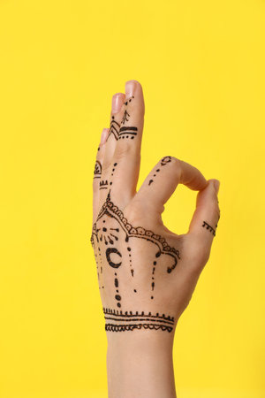 Woman with henna tattoo on hand against yellow background, closeup. traditional mehndi ornamentの写真素材