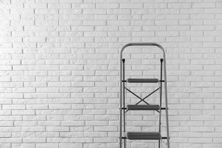 Modern metal stepladder against white brick background. Space for textの写真素材