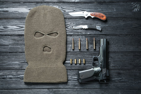 Flat lay composition with balaclava and weapons on black wooden table