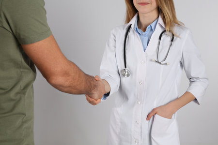 Doctor and patient shaking hands on light gray background, closeupの写真素材