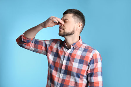 Man suffering from runny nose on light blue backgroundの写真素材