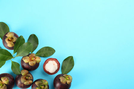 Fresh ripe mangosteen fruits with green leaves on turquoise background, flat lay. Space for textの写真素材