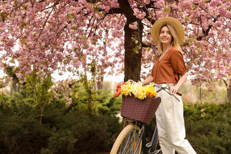 Beautiful young woman with bicycle and flowers in park on pleasant spring day. Space for textの写真素材