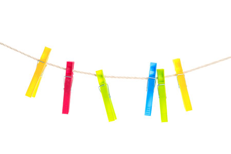 Colorful plastic clothespins hanging on rope against white backgroundの写真素材