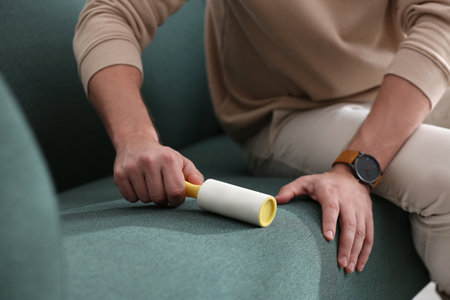Man cleaning sofa with lint roller indoors, closeupの写真素材