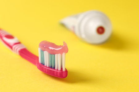 Pink brush with toothpaste on yellow background, closeup. Space for textの写真素材
