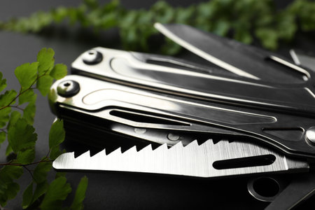 Compact portable metallic multitool and green leaves on black background, closeupの写真素材