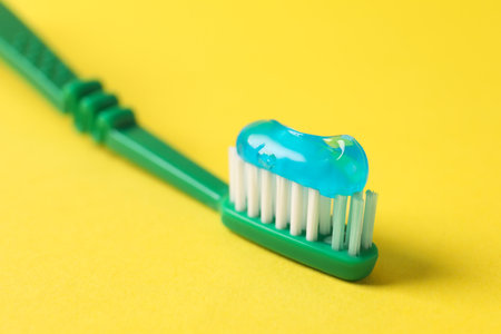 Green brush with toothpaste on yellow background, closeupの写真素材