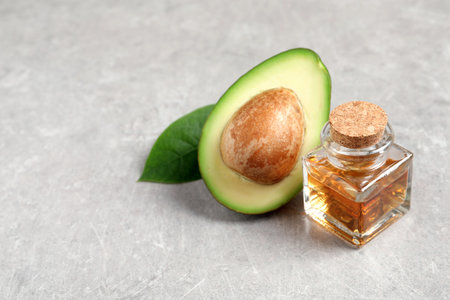 Bottle of essential oil and fresh avocado on gray table, space for textの写真素材