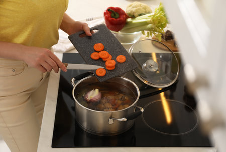 Woman putting carrot into pot to make bouillon in kitchen, closeup. homemade recipeの写真素材