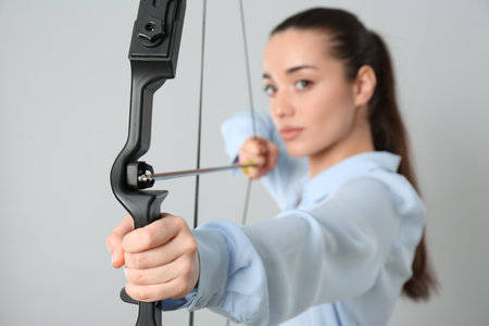 Young woman practicing archery against light gray background, focus on bowの写真素材
