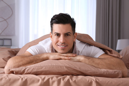 Man lying in comfortable bed with beige linesの写真素材