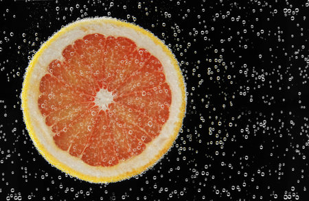 Slice of grapefruit in sparkling water on black background. Citrus sodaの写真素材
