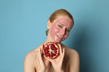 Young woman with pomegranate face mask and fresh fruit on light blue backgroundの写真素材