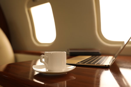 Cup of coffee with laptop and notebooks on table in airplaneの写真素材