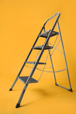 Modern metal stepladder on yellow background. construction toolの写真素材