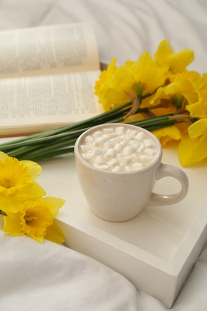 Beautiful daffodils and cup of hot drink on bedの写真素材