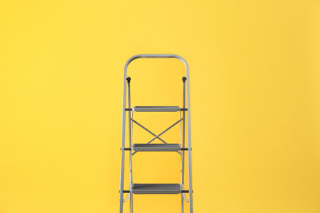 Modern metal stepladder on yellow background. construction toolの写真素材