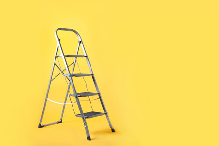 Modern metal stepladder on yellow background. Space for textの写真素材