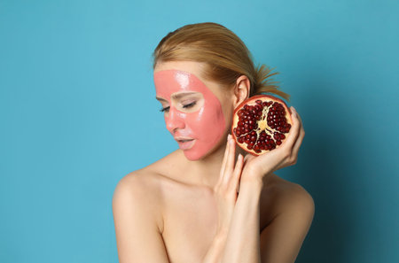 Young woman with pomegranate face mask and fresh fruit on light blue backgroundの写真素材