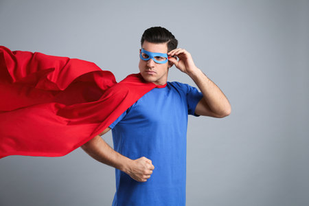 Man wearing superhero cape and mask on gray backgroundの写真素材