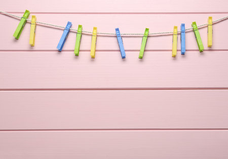 Colorful plastic clothespins and rope on pink wooden background. Space for textの写真素材