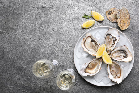 Fresh oysters with lemon, rosemary and glasses of champagne on gray table, flat lay. Space for textの写真素材