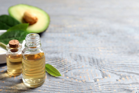 Bottles of essential oil and fresh avocado on gray wooden table, space for textの写真素材