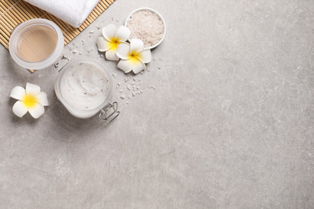 Body scrub, sea salt and plumeria flowers on gray table, flat lay. Space for textの写真素材