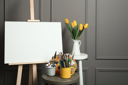 Easel with blank canvas, brushes, paints and palette in studioの写真素材