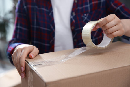 Woman taping cardboard box indoors, closeup. moving dayの写真素材