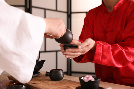 Master pouring freshly brewed beverage into guest's cup during traditional tea ceremony at table, closeupの写真素材