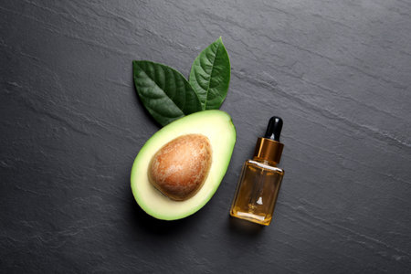 Bottle of essential oil, green leaves and fresh avocado on black table, flat layの写真素材