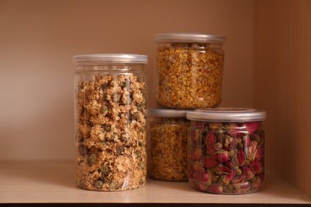 Glass jars with different dry herbs for tea on wooden shelfの写真素材