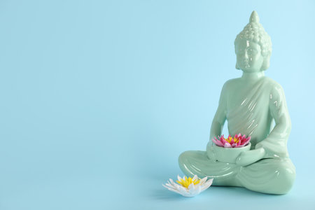 Beautiful ceramic Buddha sculpture with flowers on light blue background. Space for textの写真素材