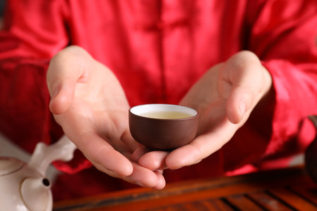 Master offering cup of freshly brewed beverage during traditional tea ceremony at table, closeupの写真素材