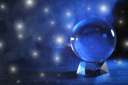 Magic crystal ball on table and smoke against dark background, space for text. Making predictionsの写真素材