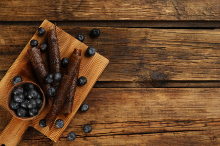 Delicious fruit leather rolls and blueberries on wooden table, flat lay. Space for textの写真素材