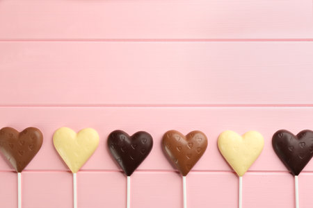Different chocolate heart shaped lollipops on pink wooden table, flat lay. Space for textの写真素材