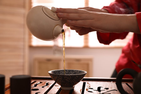 Master pouring freshly brewed beverage into cup during traditional tea ceremony at table, closeupの写真素材